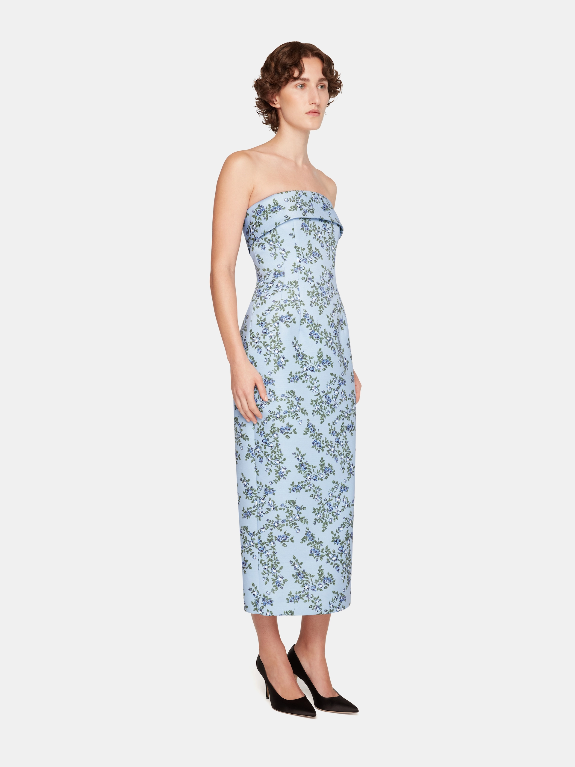 Woman wearing strapless light blue Emilia Wickstead floral midi dress with folded neckline and black high heels.