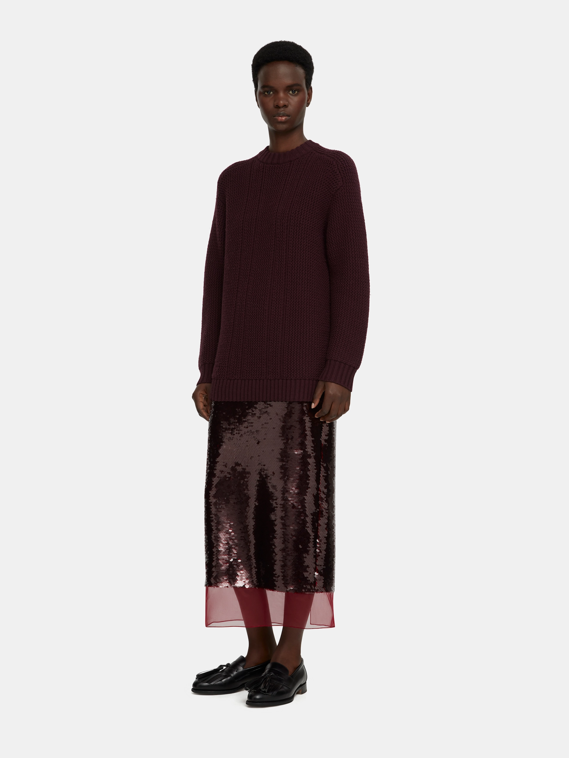 Model wearing a dark purple Emilia Wickstead knit sweater, sequined skirt with sheer hem, and black loafers.
