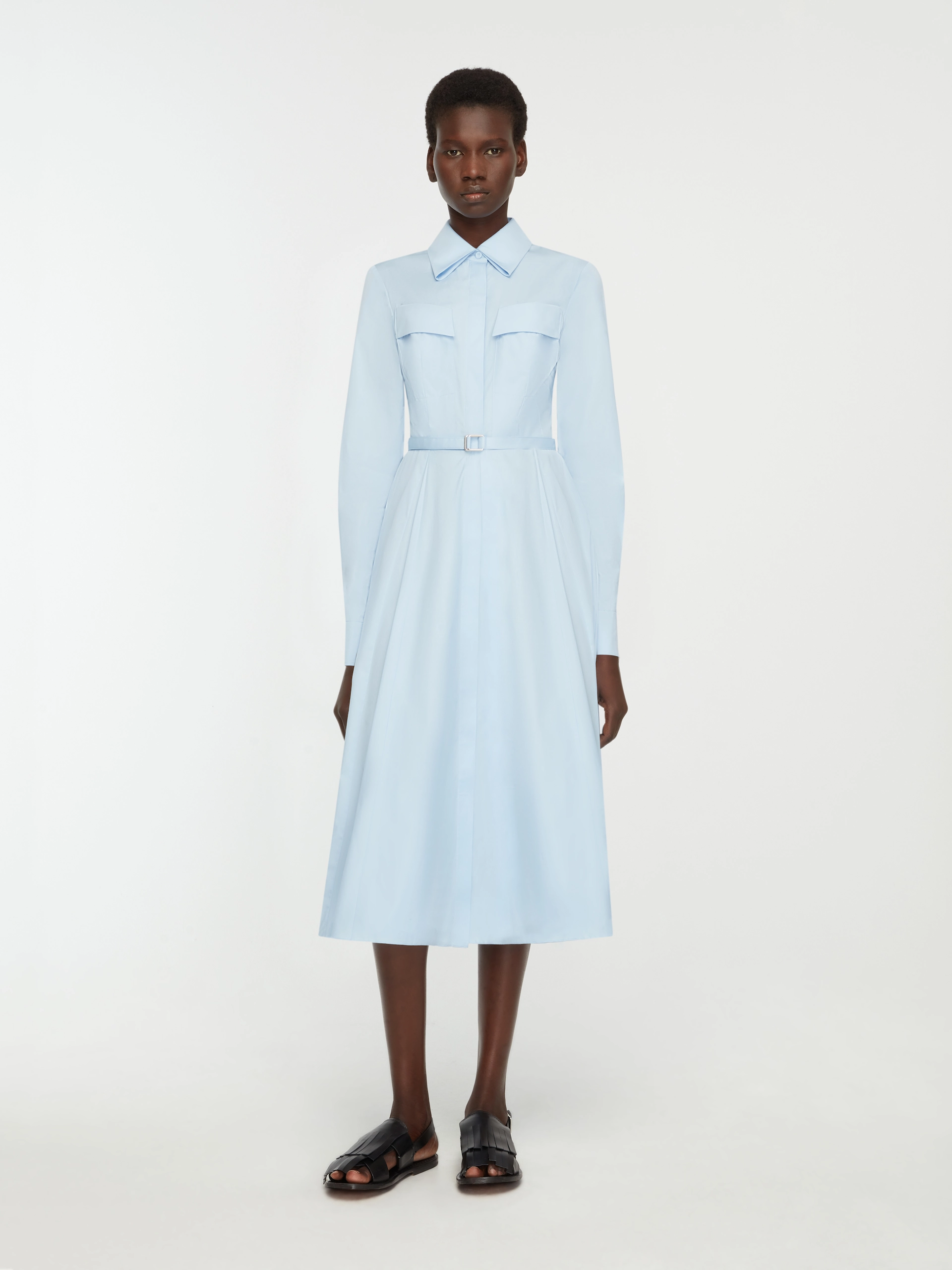 Woman wearing a light blue belted Emilia Wickstead midi dress with long sleeves and black sandals.