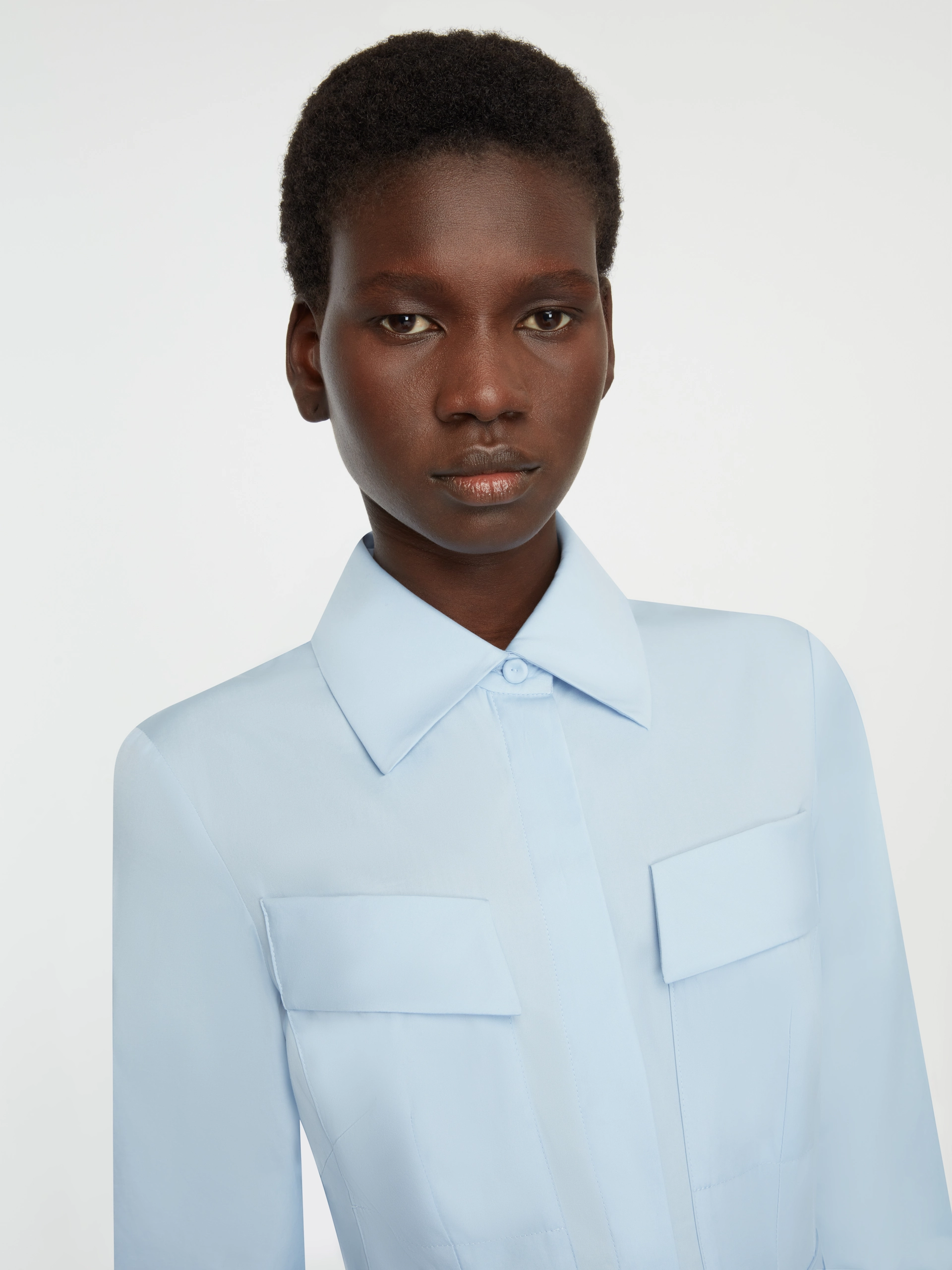 Woman with short hair wearing a light blue collared Emilia Wickstead shirt with flap pockets.