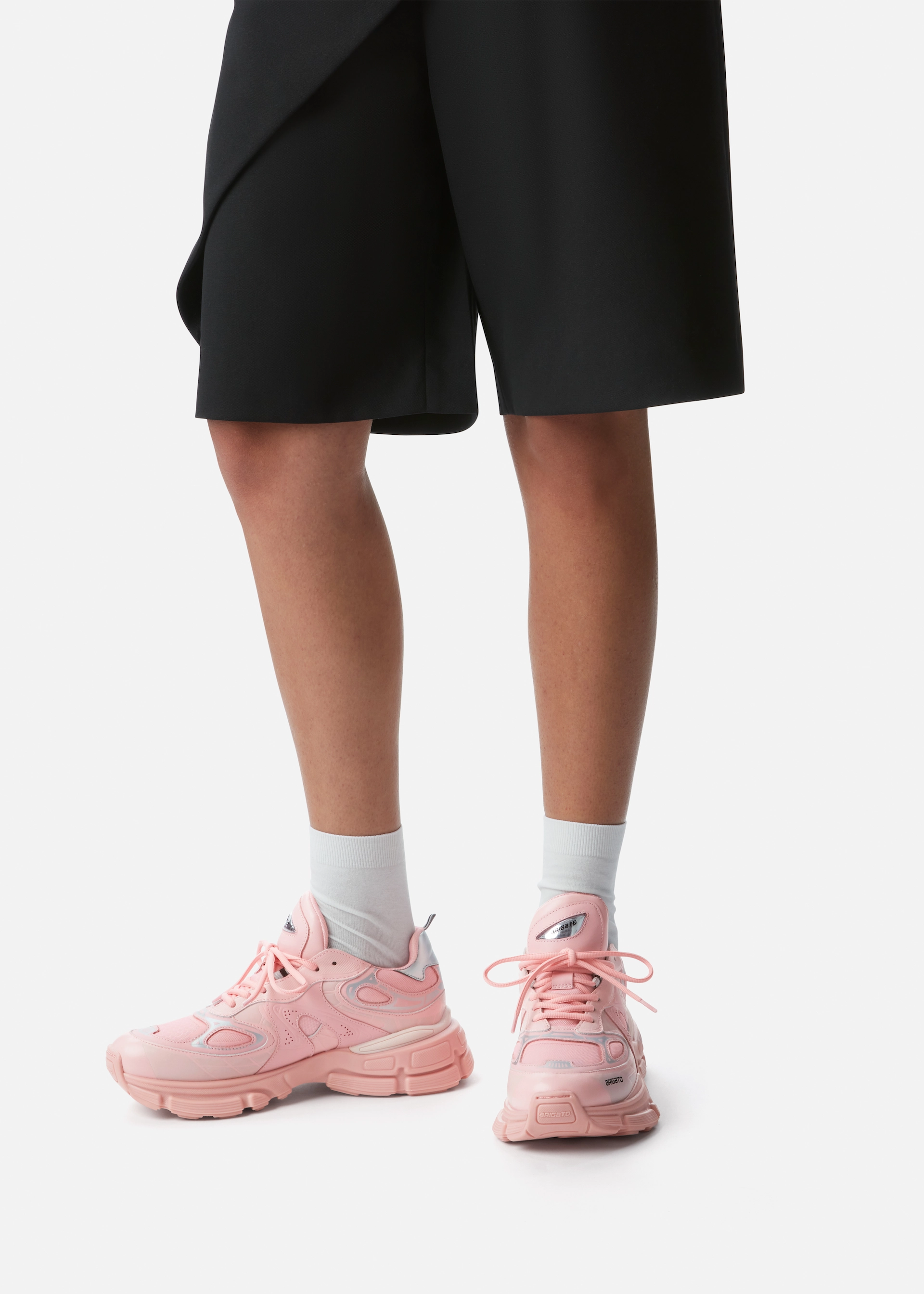 Person wearing black shorts and white socks with pink chunky sneakers on a white background.