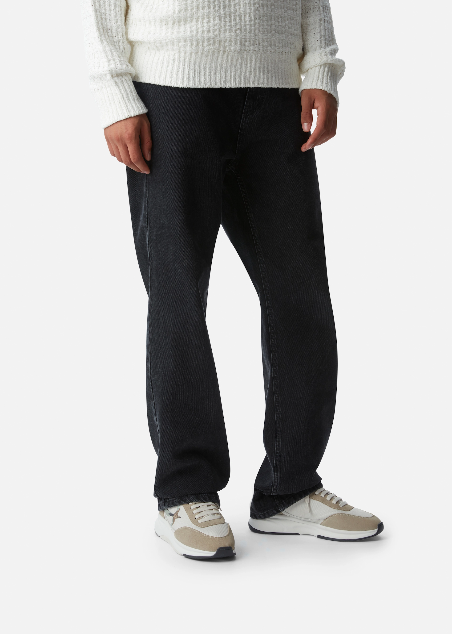 Person wearing loose black jeans, beige and white Axel Arigato sneakers, and a white textured sweater.