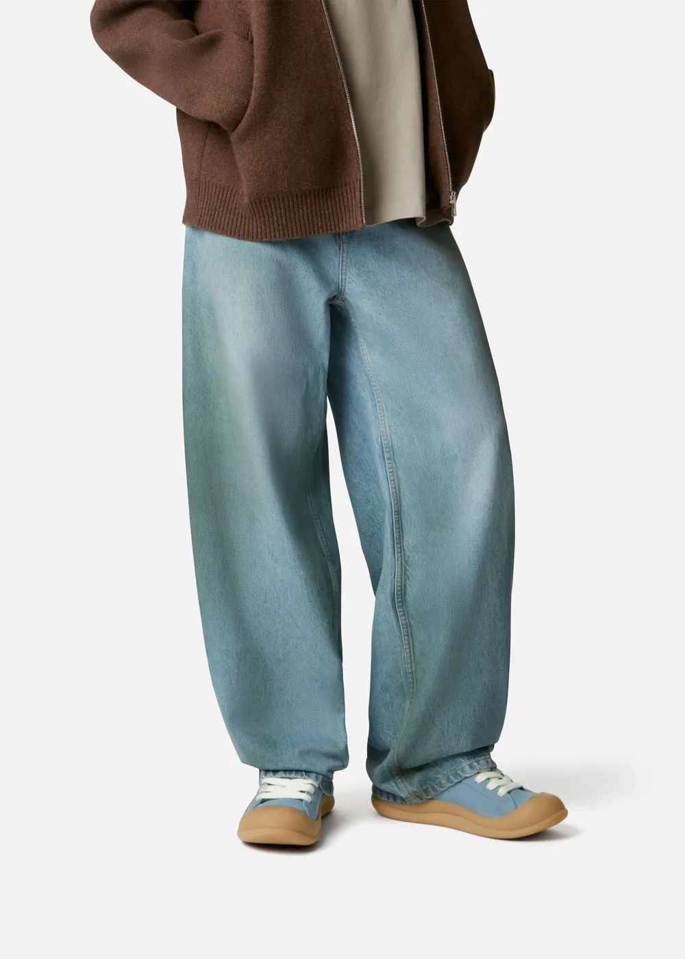 Person wearing baggy light blue jeans, a brown zip jacket, and light blue Axel Arigato  sneakers with gum soles.