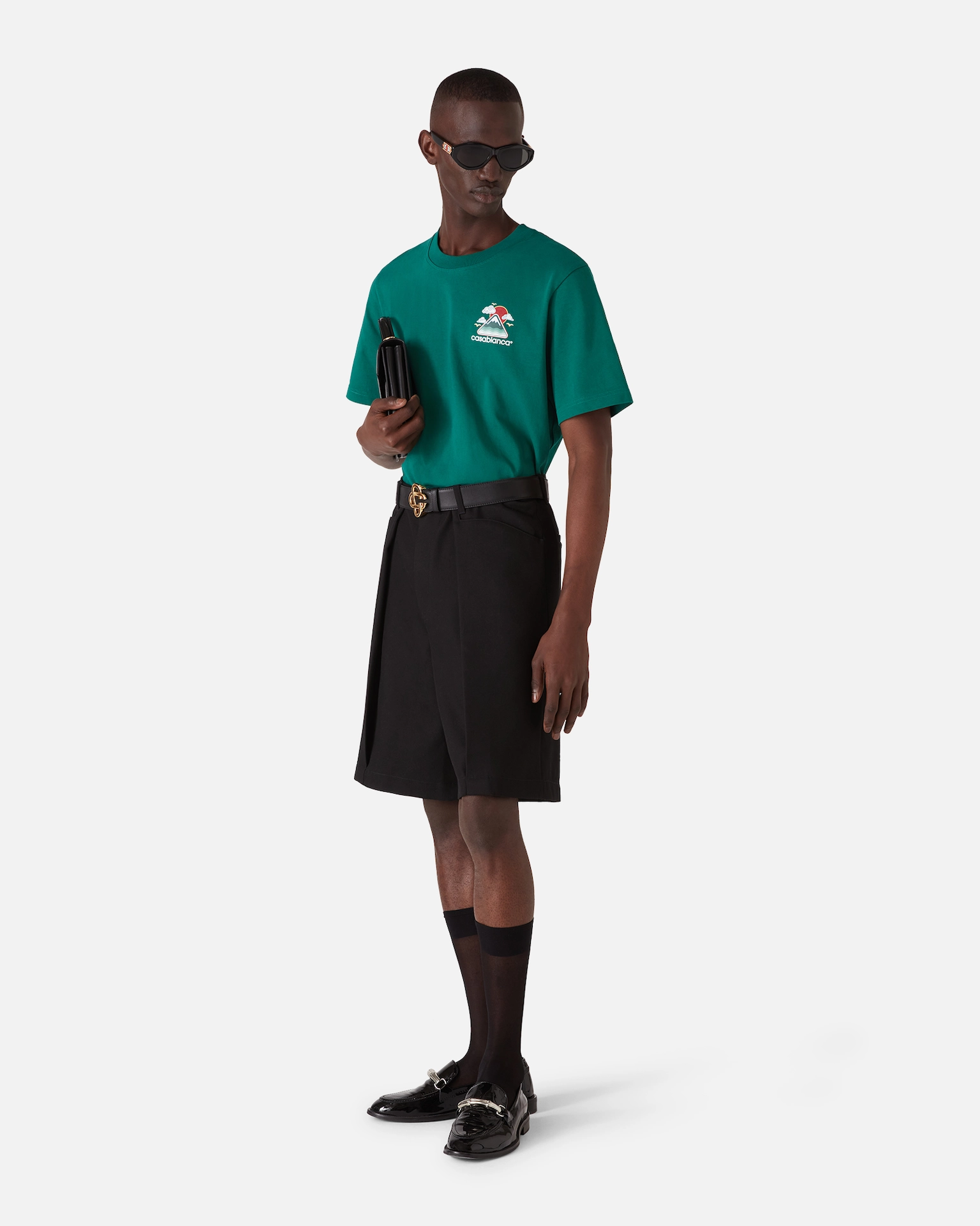 Man wearing green Casablanca t-shirt, black shorts, black belt, sheer black socks, and black loafers with sunglasses.