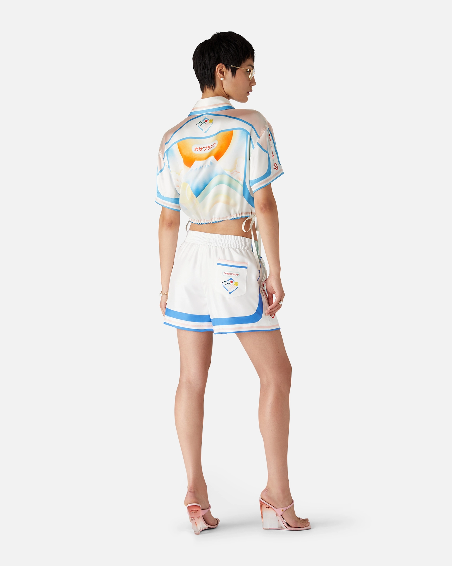 Rear view of woman wearing a white and blue matching Casablanca short set with graphic design and pink wedge heels.