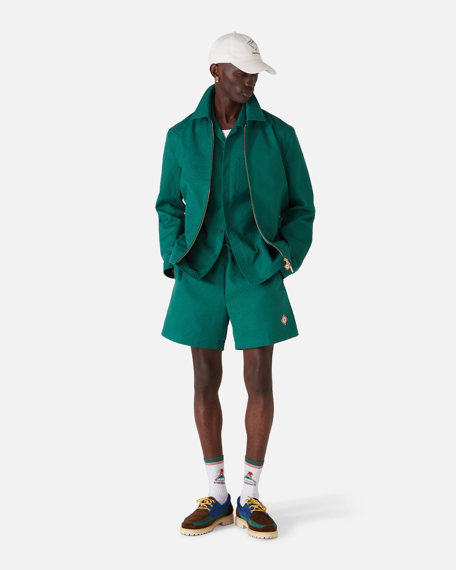 Man wearing green Casablanca jacket, matching shorts, white cap, colorful shoes, and white patterned socks.