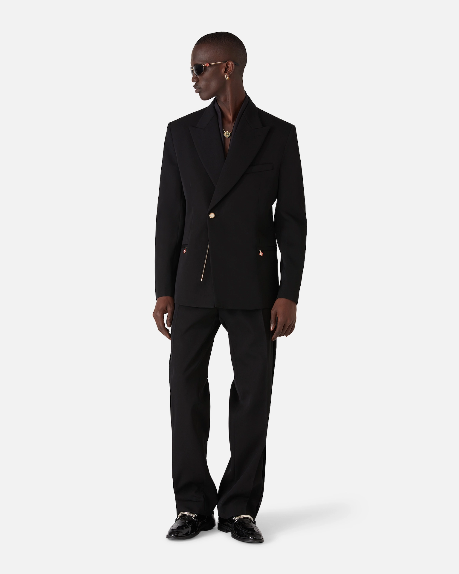 Man wearing a black Casablanca suit with gold buttons, black pants, and black dress shoes looking to the side.