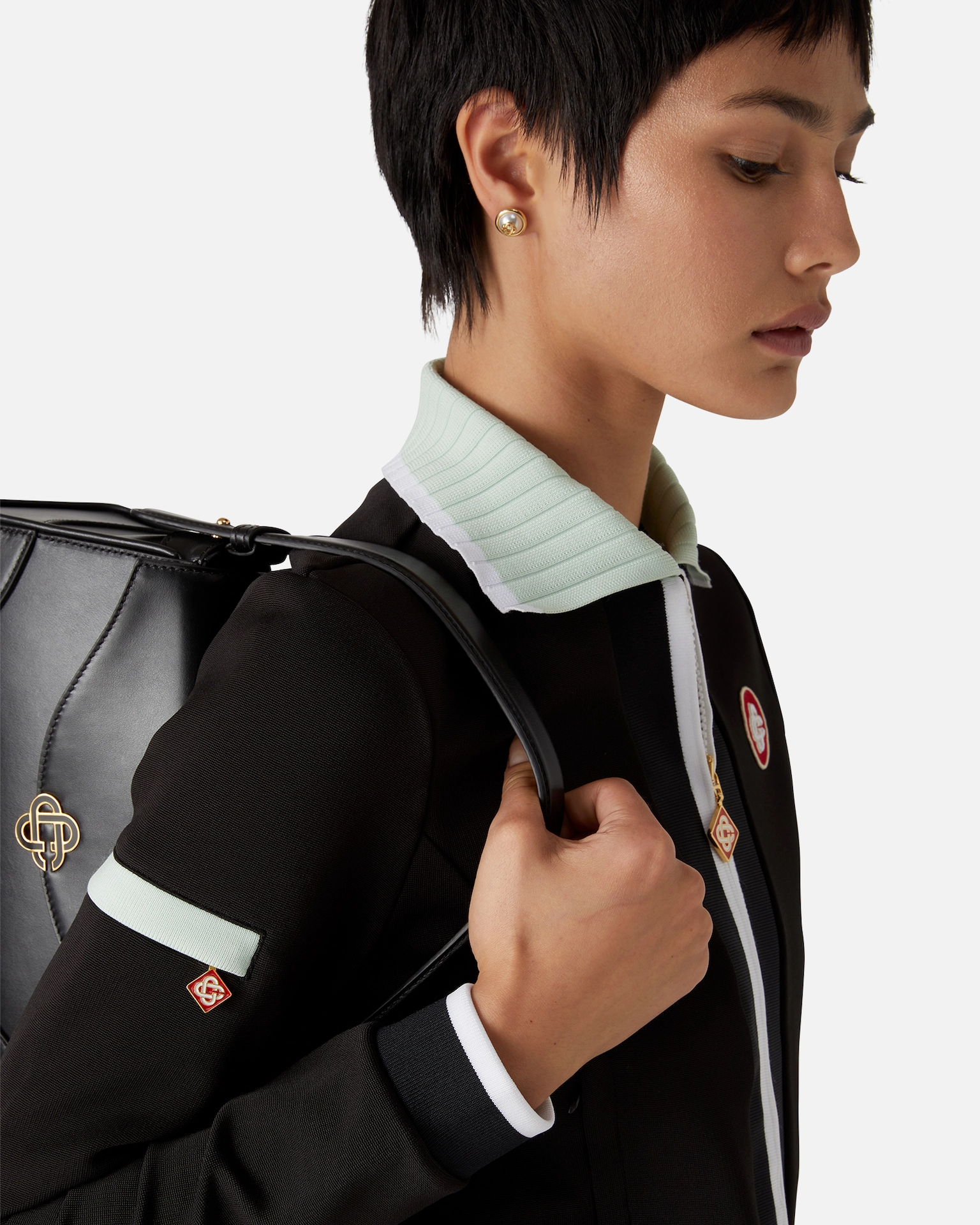 Close-up of a woman with short hair wearing pearl earrings and carrying a black Casablanca leather bag.