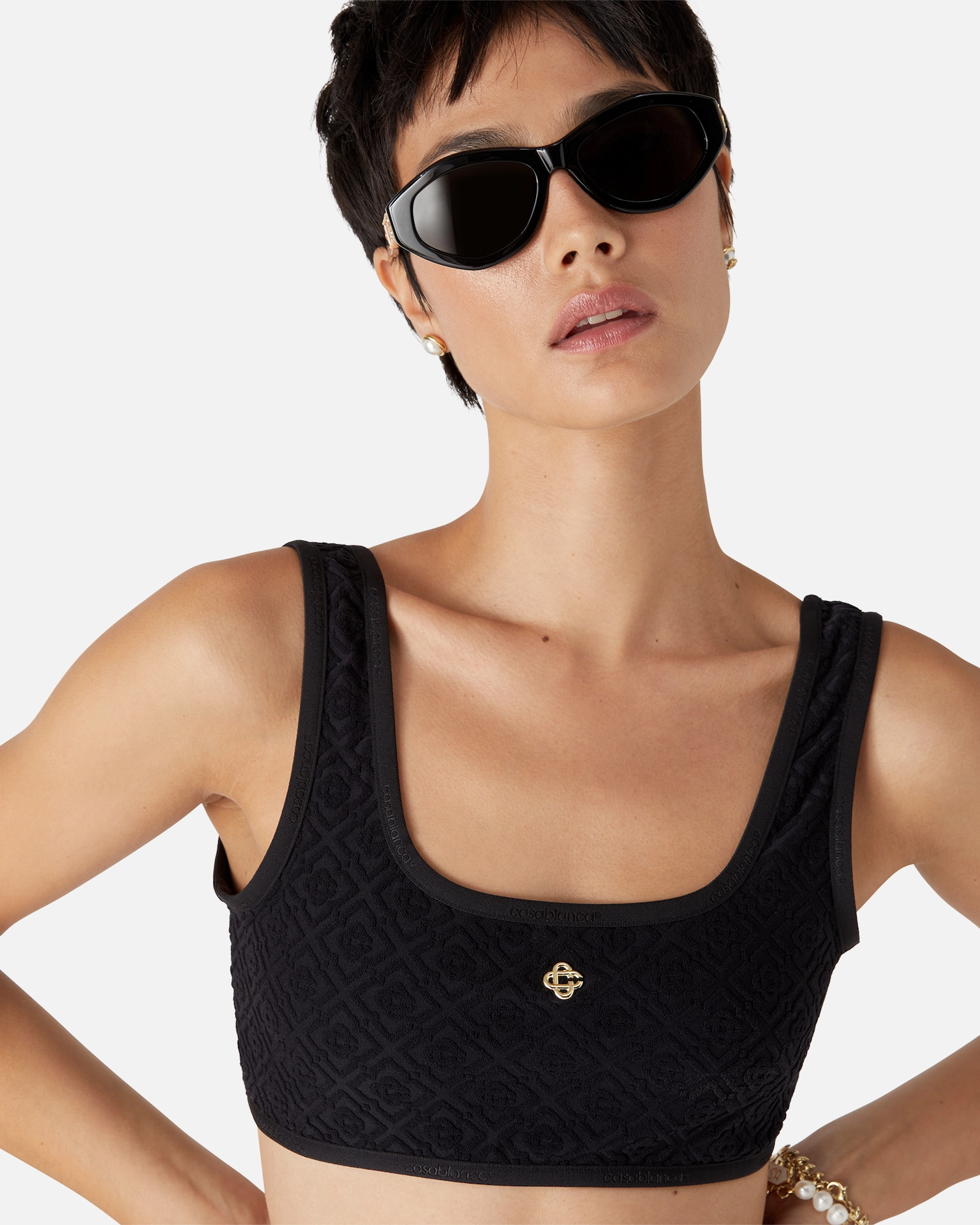 Woman with short hair wearing black Casablanca textured crop top, black sunglasses, pearl earrings, and bracelets.