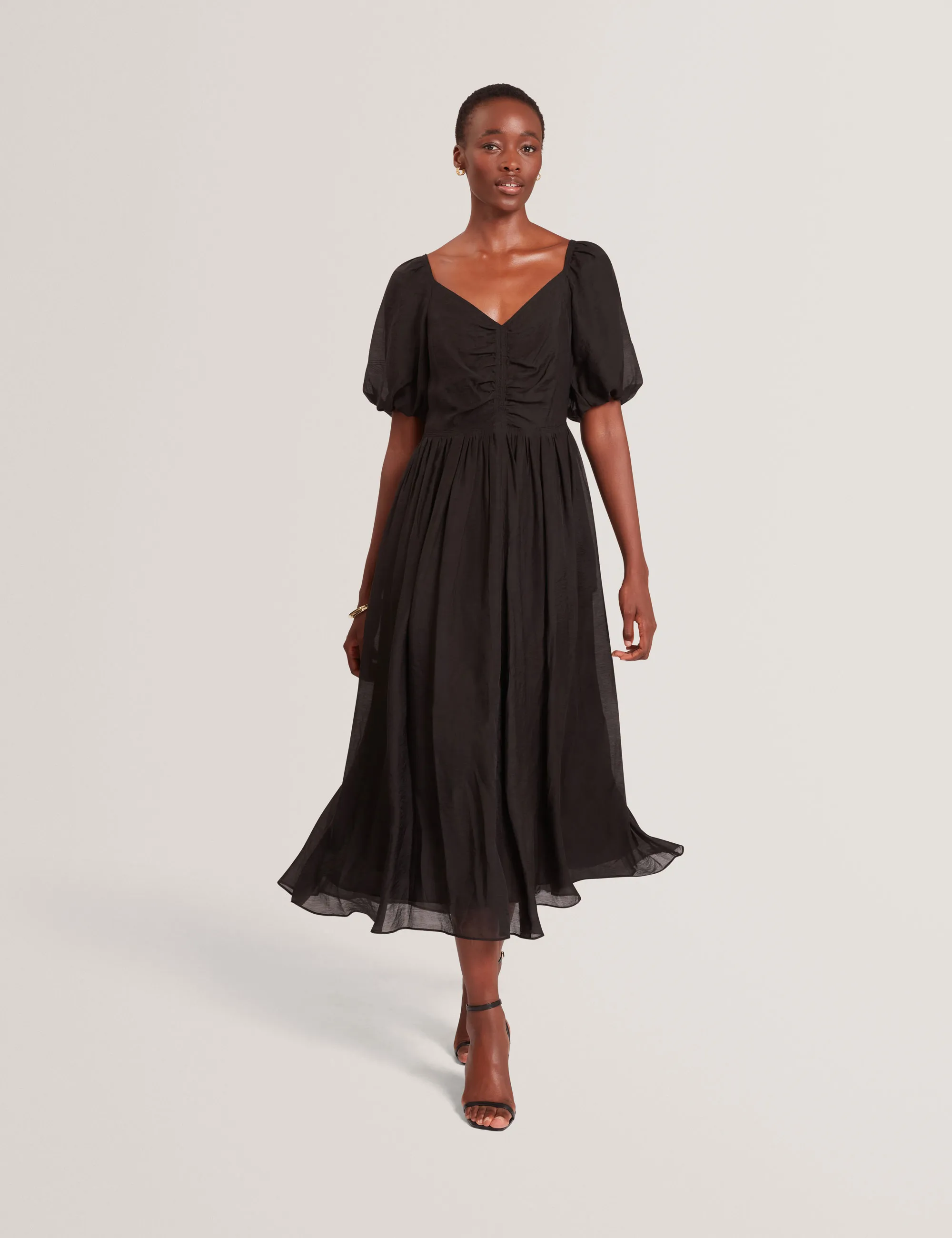 Woman wearing a flowing Ted Baker  black midi dress with puff sleeves and a V-neckline, walking forward.