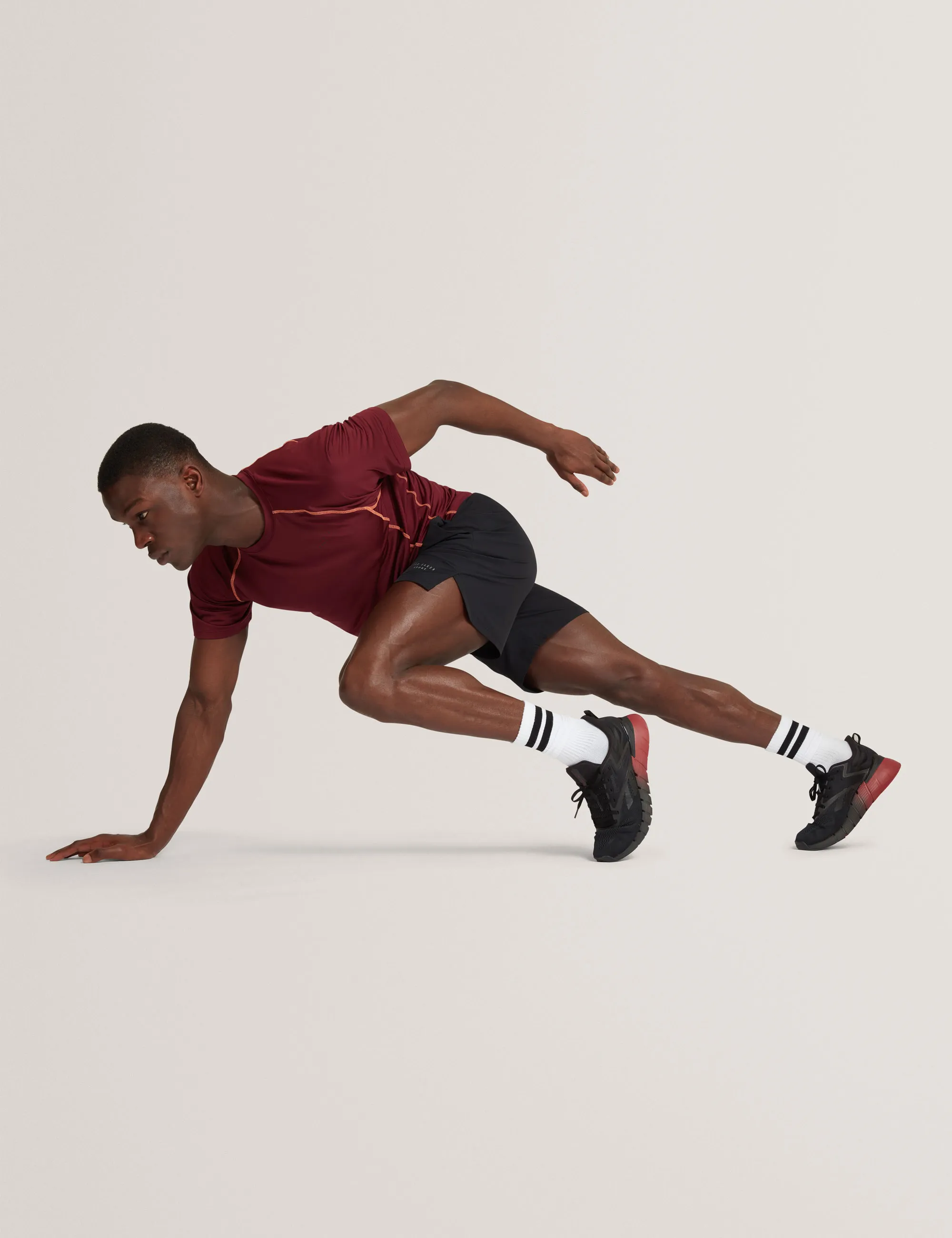 Athlete in maroon shirt and black shorts lunges forward with one hand on the ground.