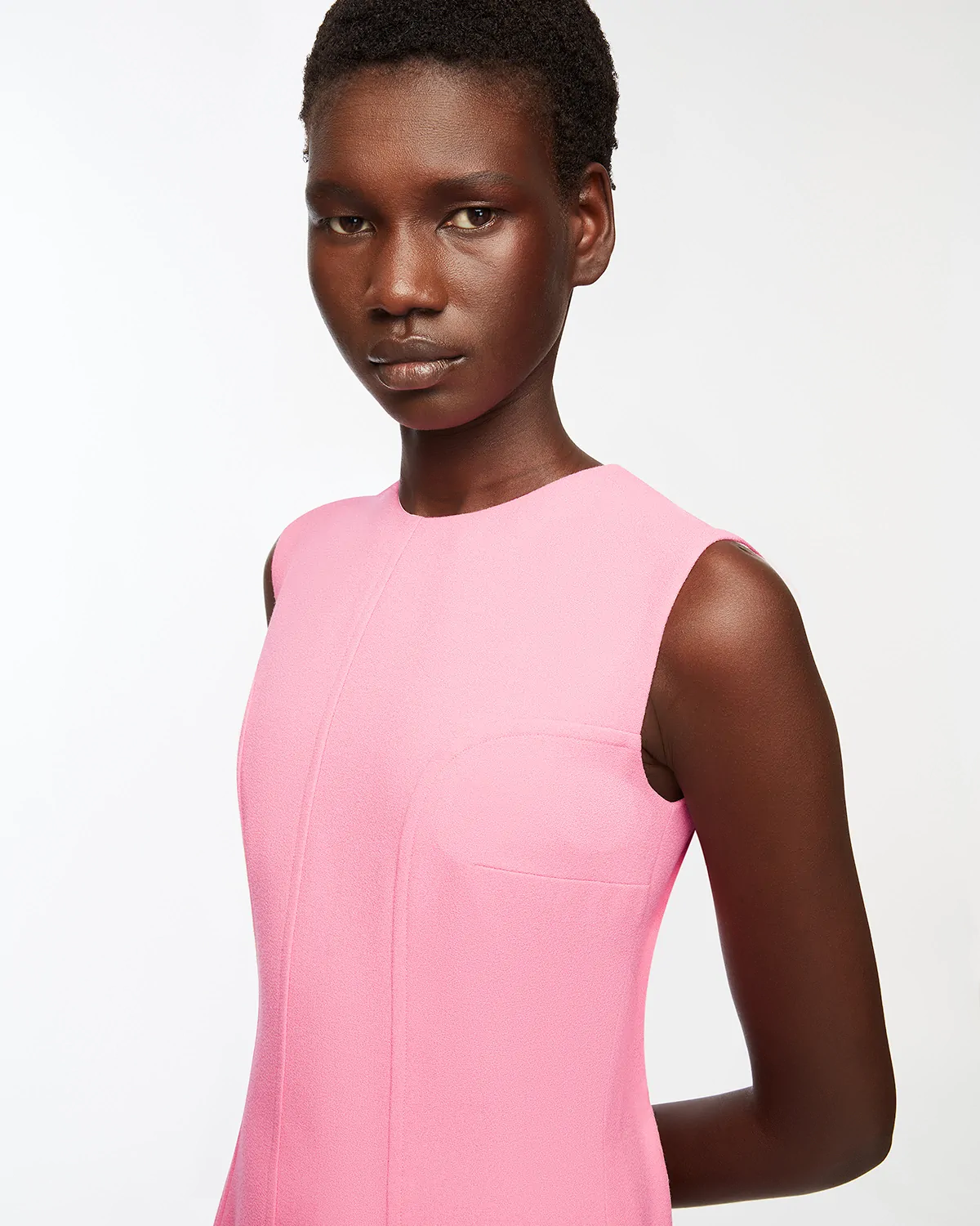 Portrait of a woman with short hair wearing an Emilia Wickstead sleeveless pink dress against a white background.
