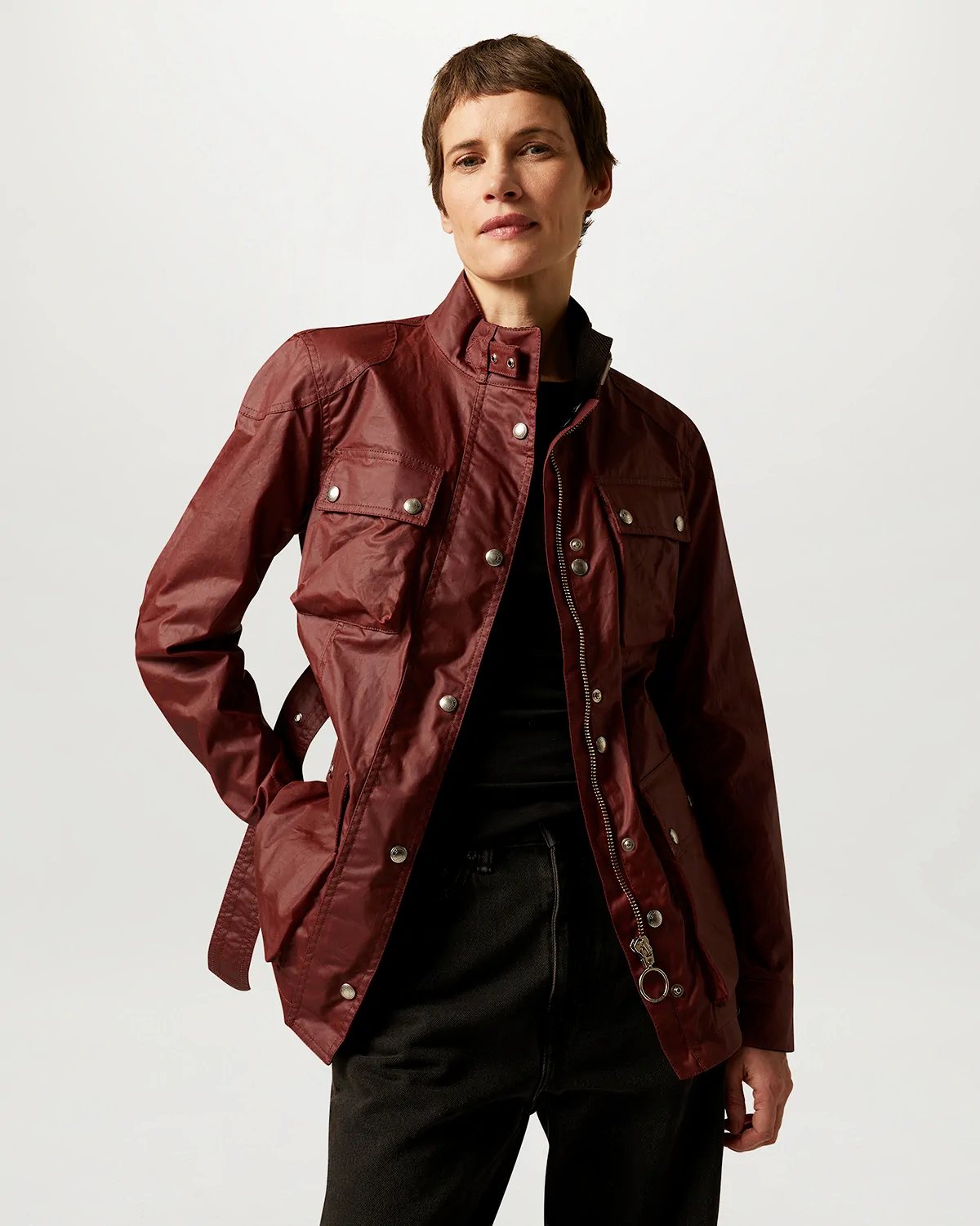 Person wearing an open deep red Belstaff jacket with front pockets and silver buttons over a black top and black pants.