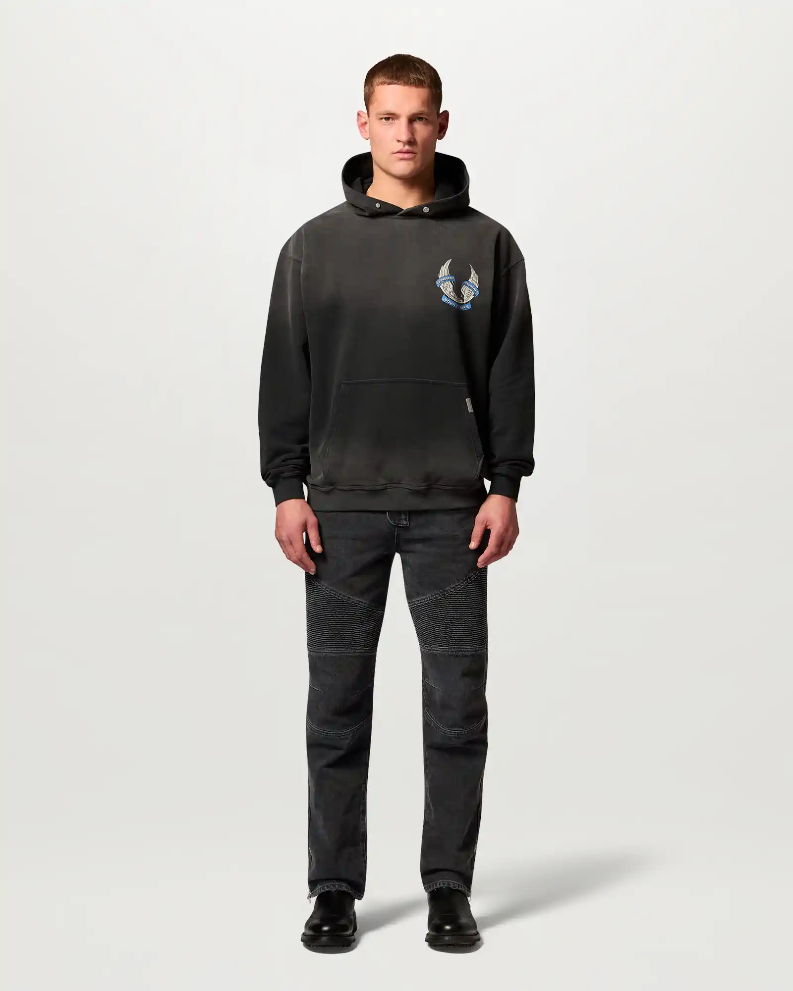 Man wearing a black Belstaff hoodie with wing graphic and matching stitched black jeans, facing forward.