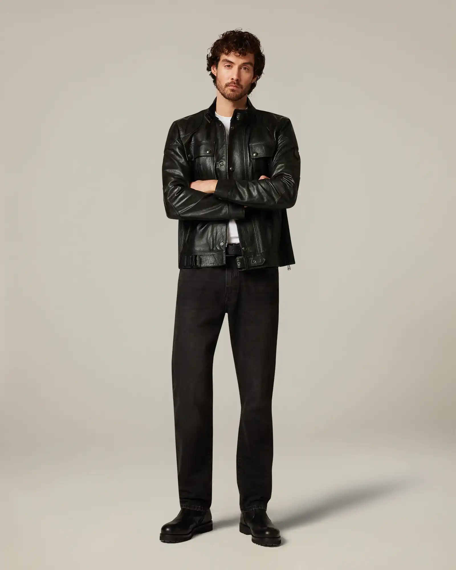 Man standing with arms crossed wearing a black leather Belstaff jacket, black pants, and black boots.