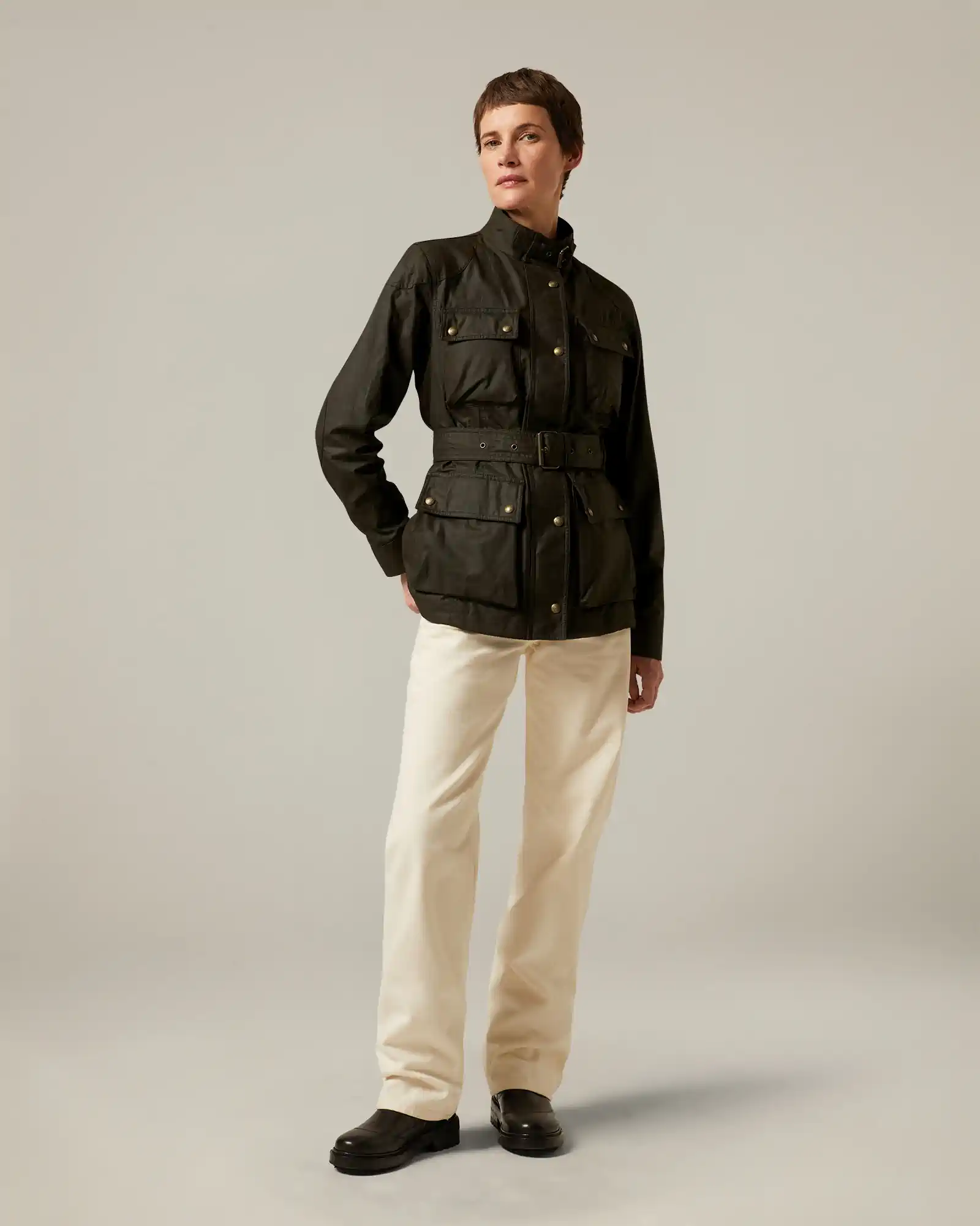 Person wearing olive Belstaff belted jacket with buttoned pockets and cream-colored pants.