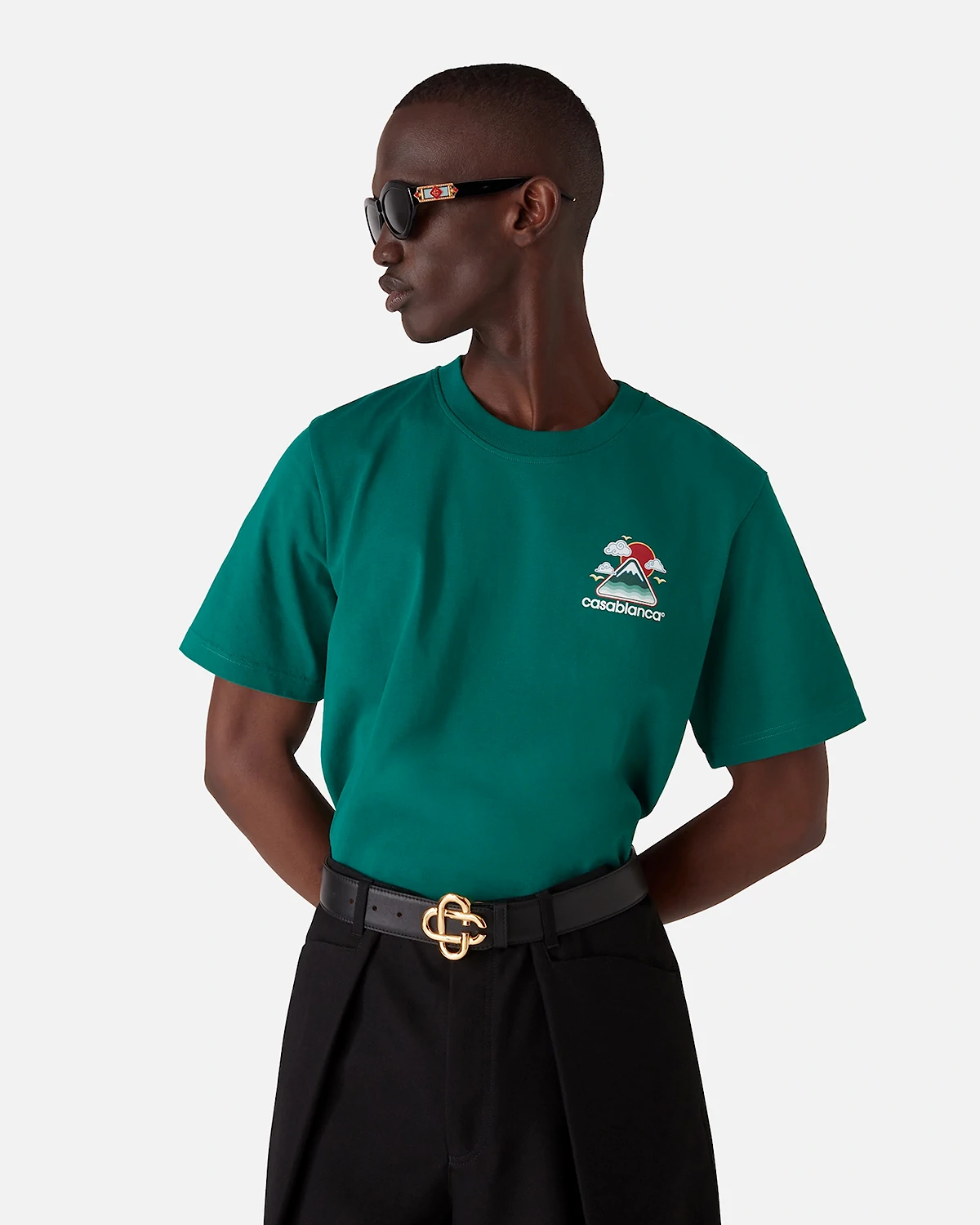 Man wearing dark green Casablanca t-shirt, black pants, black belt with gold buckle, and sunglasses.