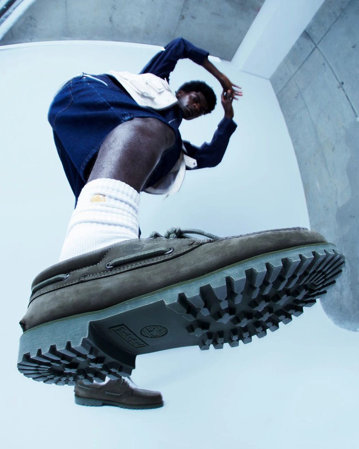 Low-angle view of a LRP model wearing brown Timberland shoes with white socks raising a leg indoors.