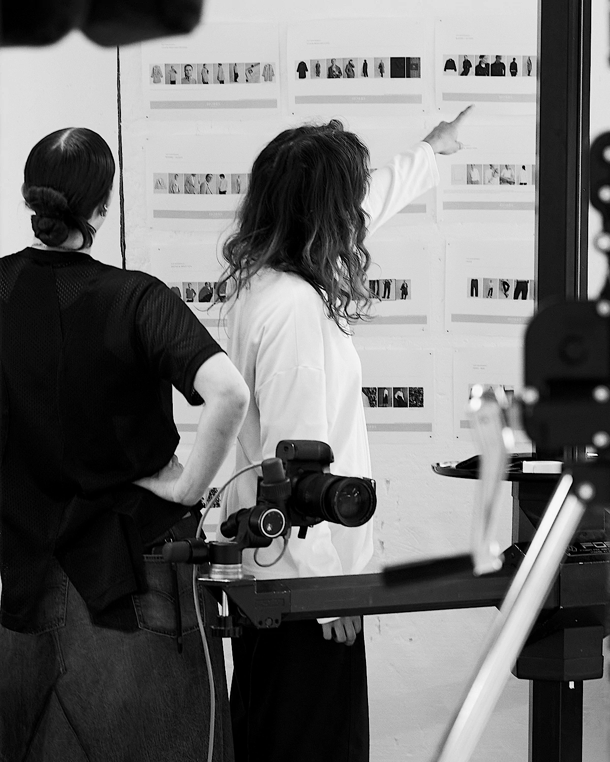 Two people review small photos taped to a wall in at. LRP e-commerce photography studio, with camera equipment nearby.