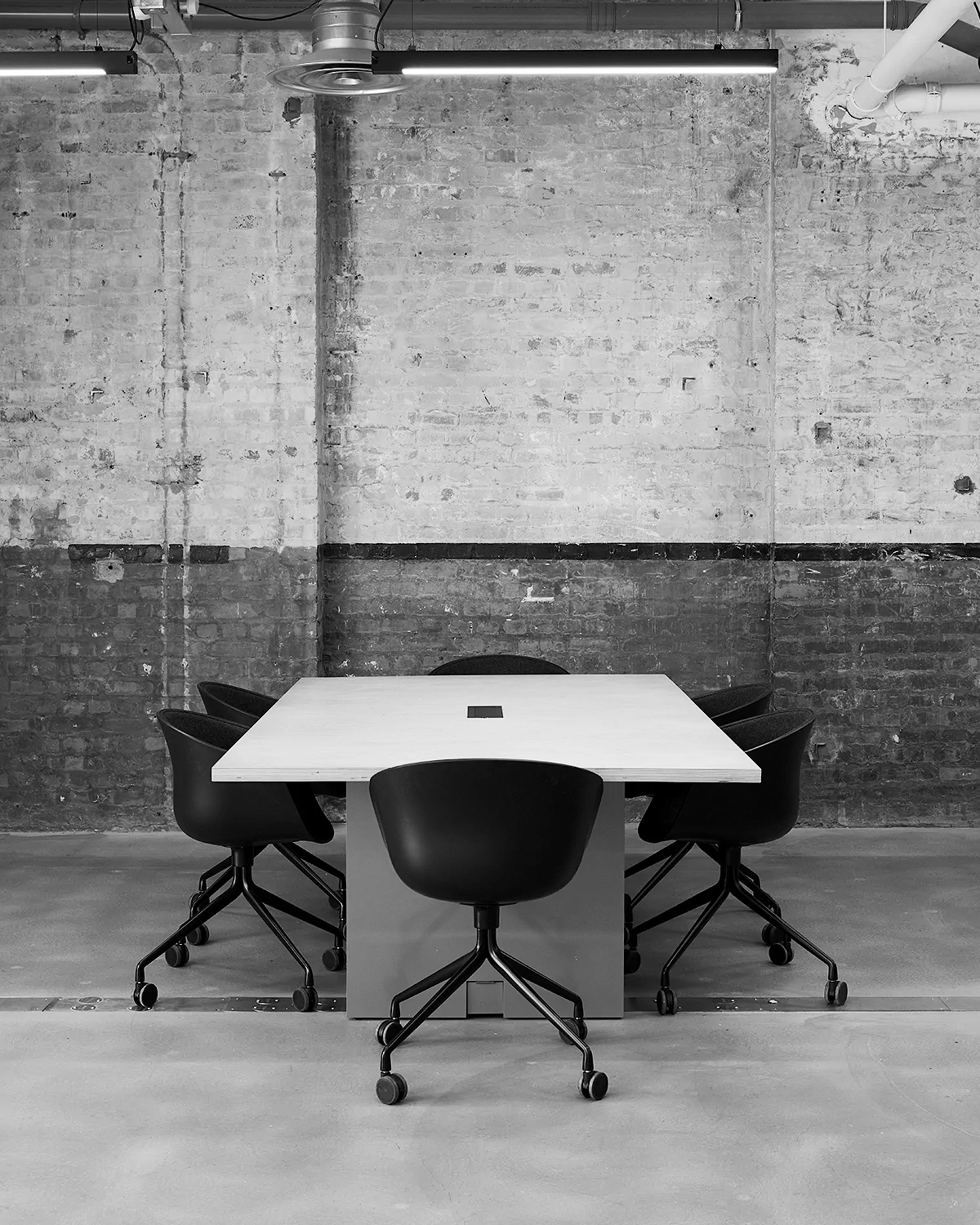 LRP meeting room with a square table and five black swivel chairs against an aged brick wall.