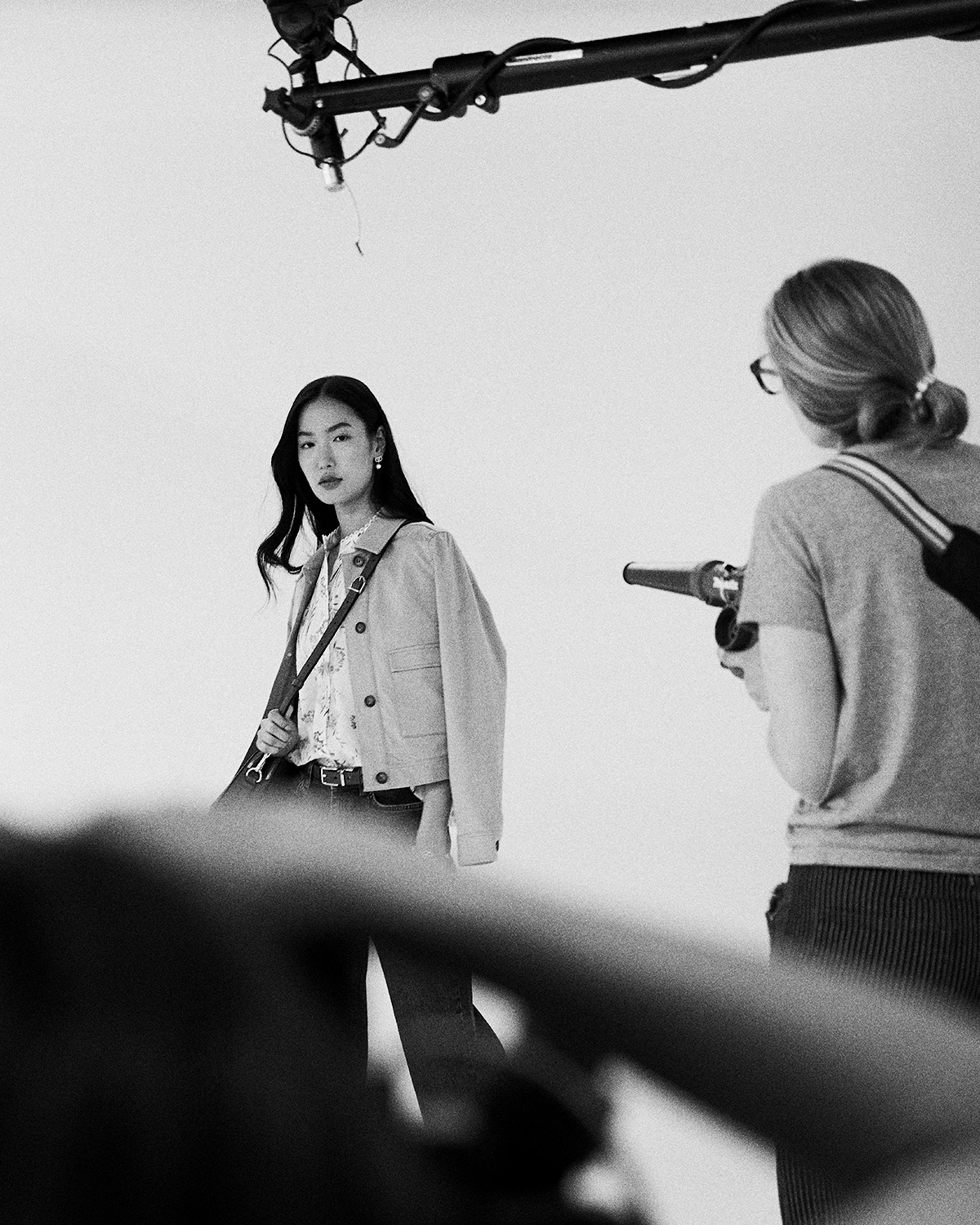 Black-and-white photo of a woman posing for a photographer holding a camera in a studio during a LRP e-commerce photography shoot.