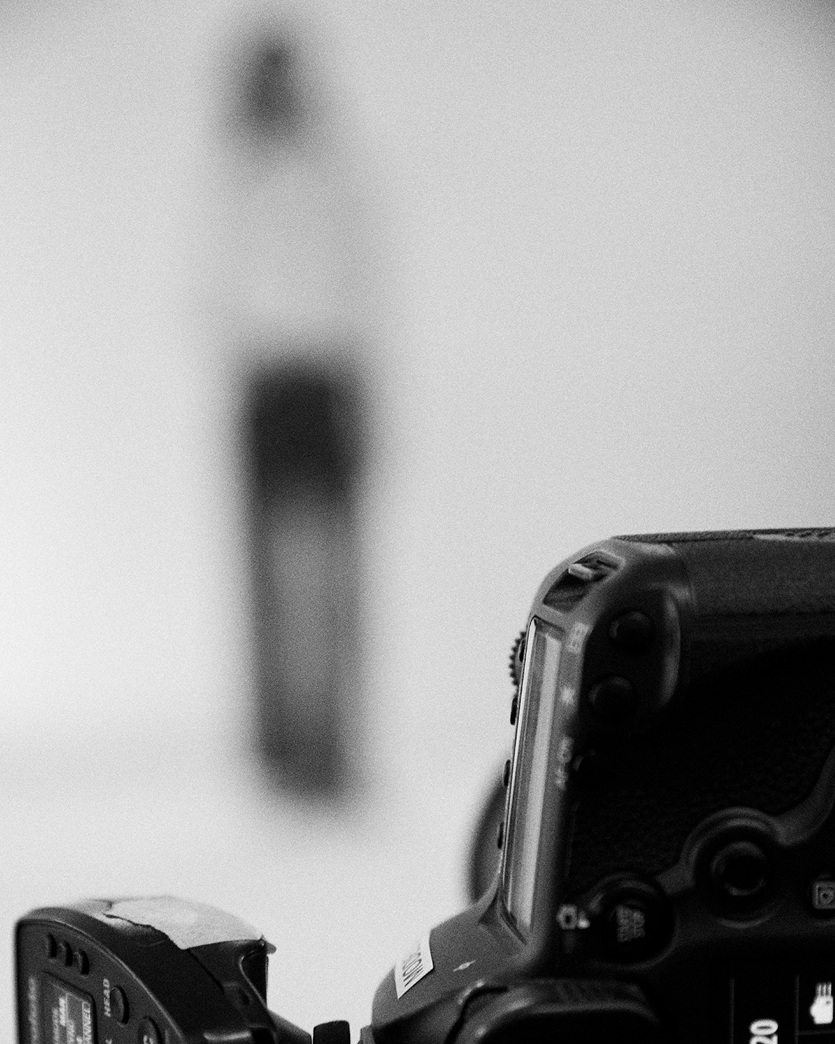 Closeup of a camera facing a blurred person posing against a plain background in black and white during an LRP studio e-commerce photoshoot.