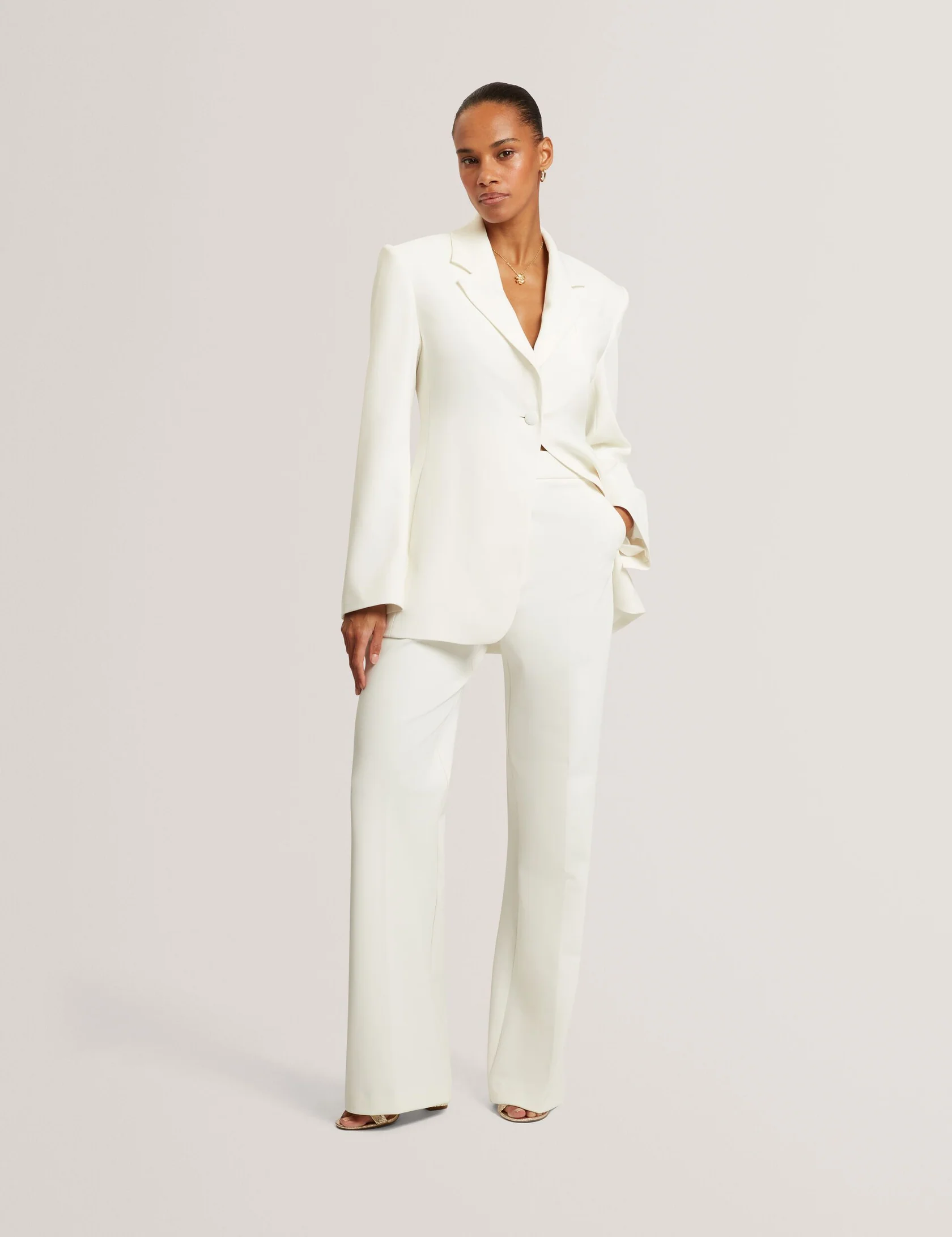 Woman in ivory tailored blazer and matching wide-leg pants posing against a plain background.