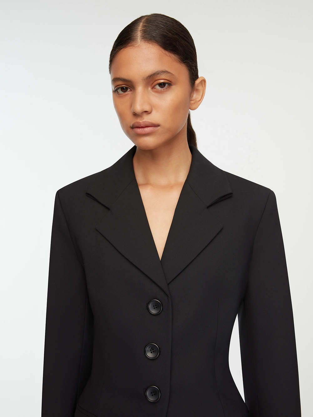 Woman with slicked-back hair wearing a black Emilia Wickstead blazer with three buttons against a white background.