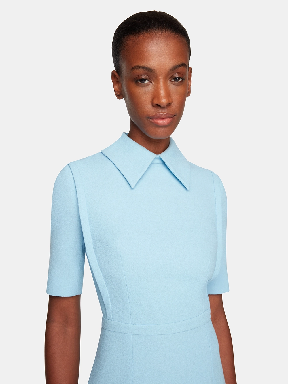 Woman wearing a light blue Emilia Wickstead dress with short sleeves and a pointed collar, against a plain background.