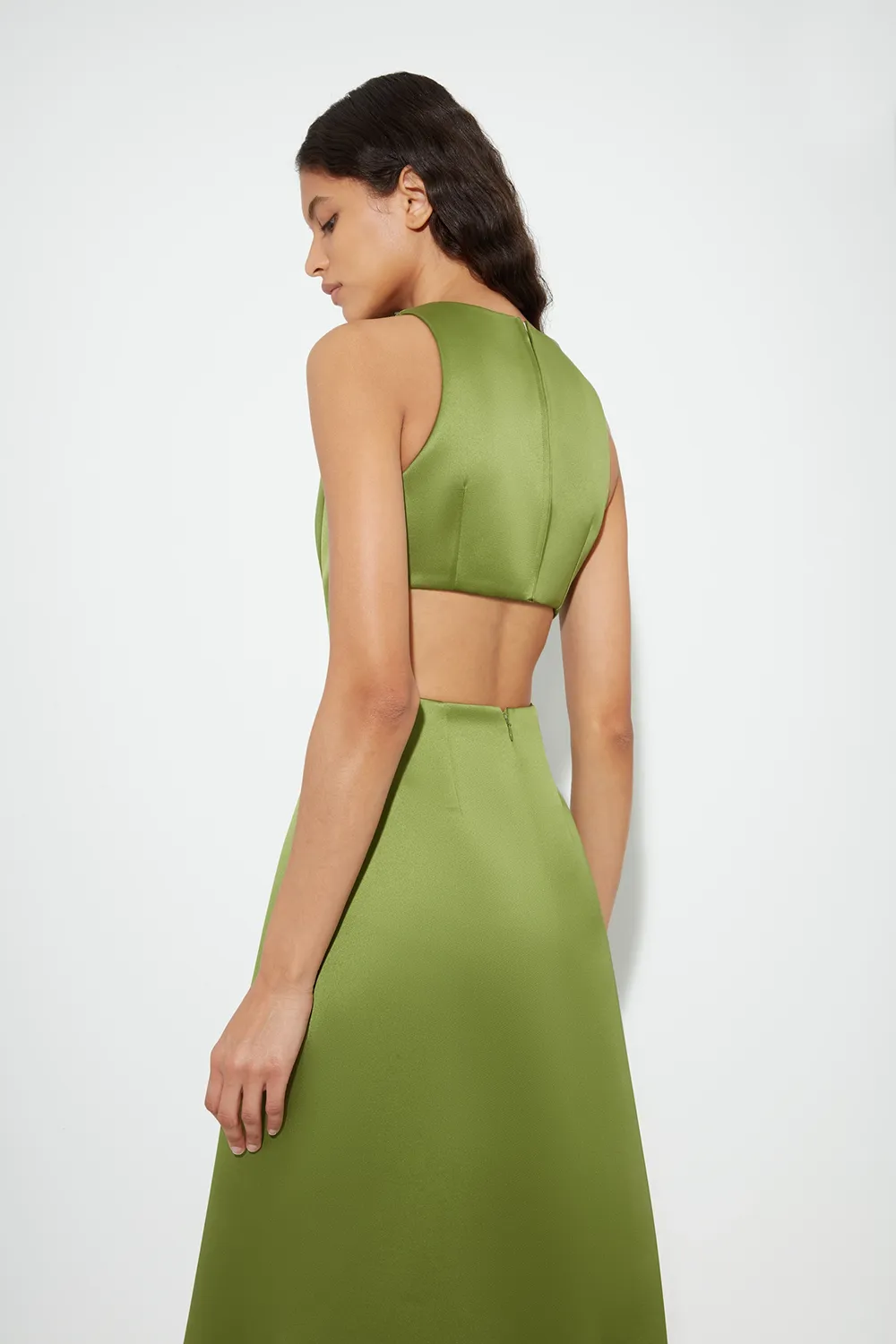 Woman with long dark hair wearing a sleeveless olive green Emilia Wickstead dress with an open back.