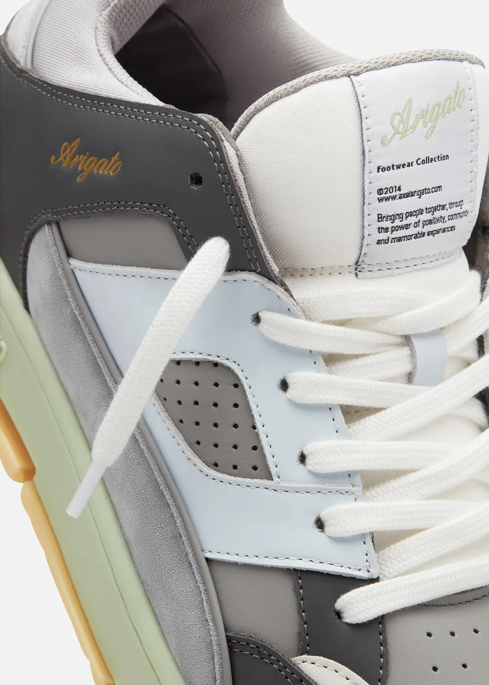 Close-up of Axel Arigato sneaker with white laces and multi-tone grey, blue, and beige panels.