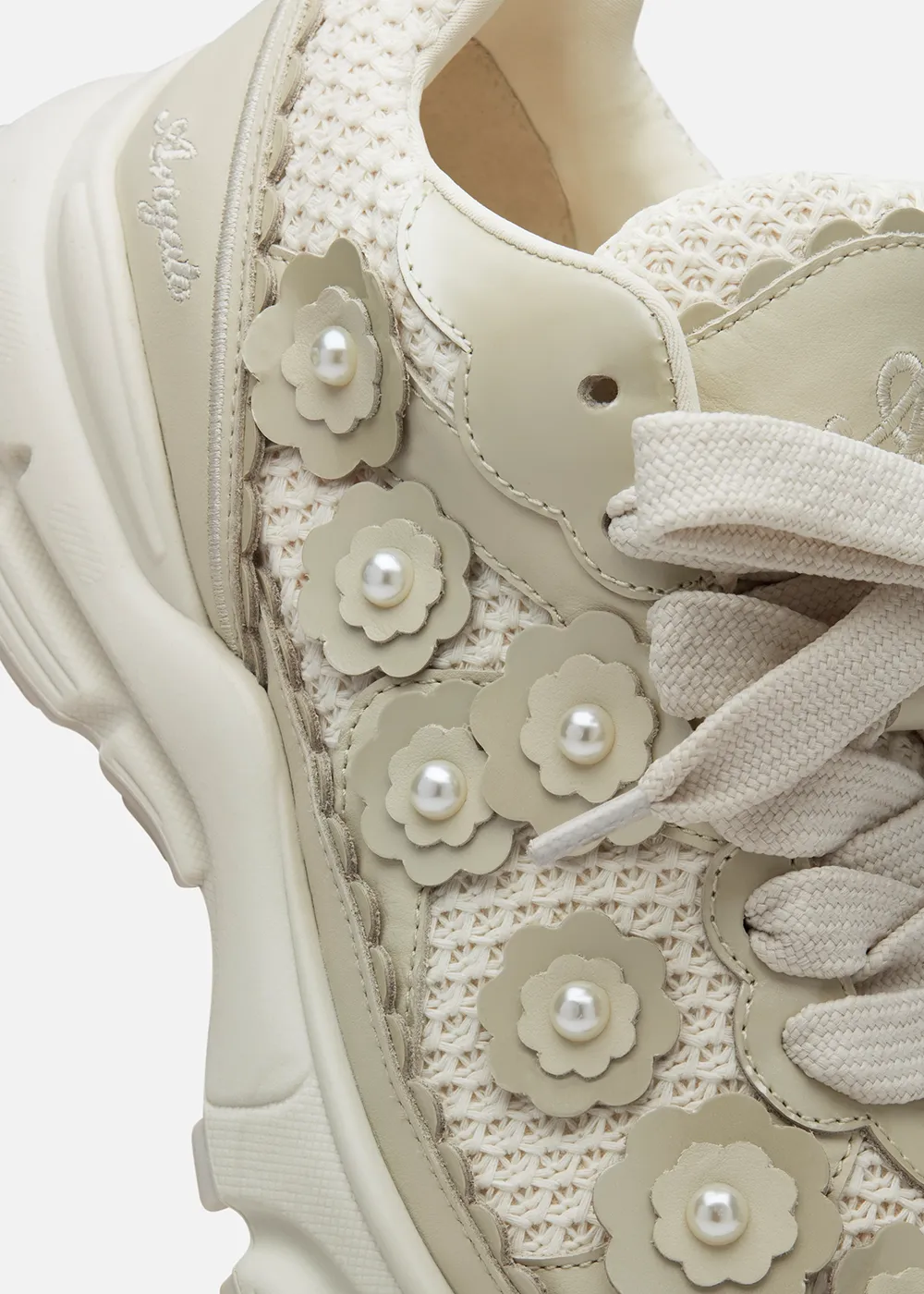 Close-up of beige Axel Arigato sneaker with floral leather appliques and pearl accents on woven fabric.