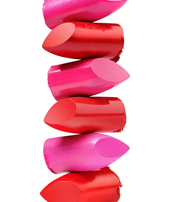 Stack of six broken lipstick tips in varying shades of red and pink on a white background.