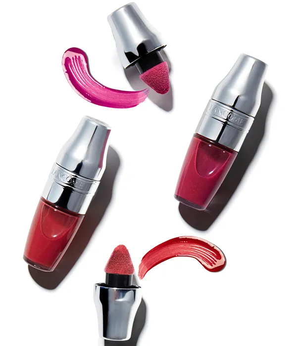 Two Lancôme lipsticks with silver caps and two matching lipstick swatches on a white background.