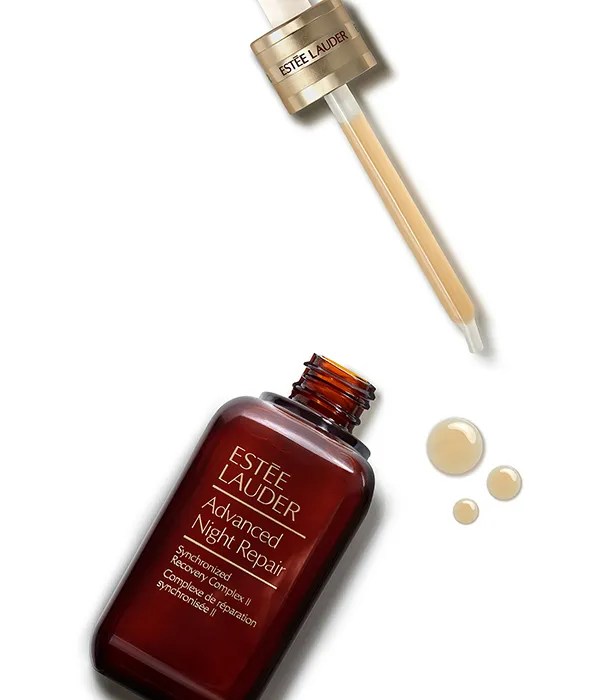 Open bottle of Estée Lauder Advanced Night Repair serum with dropper and three serum drops.