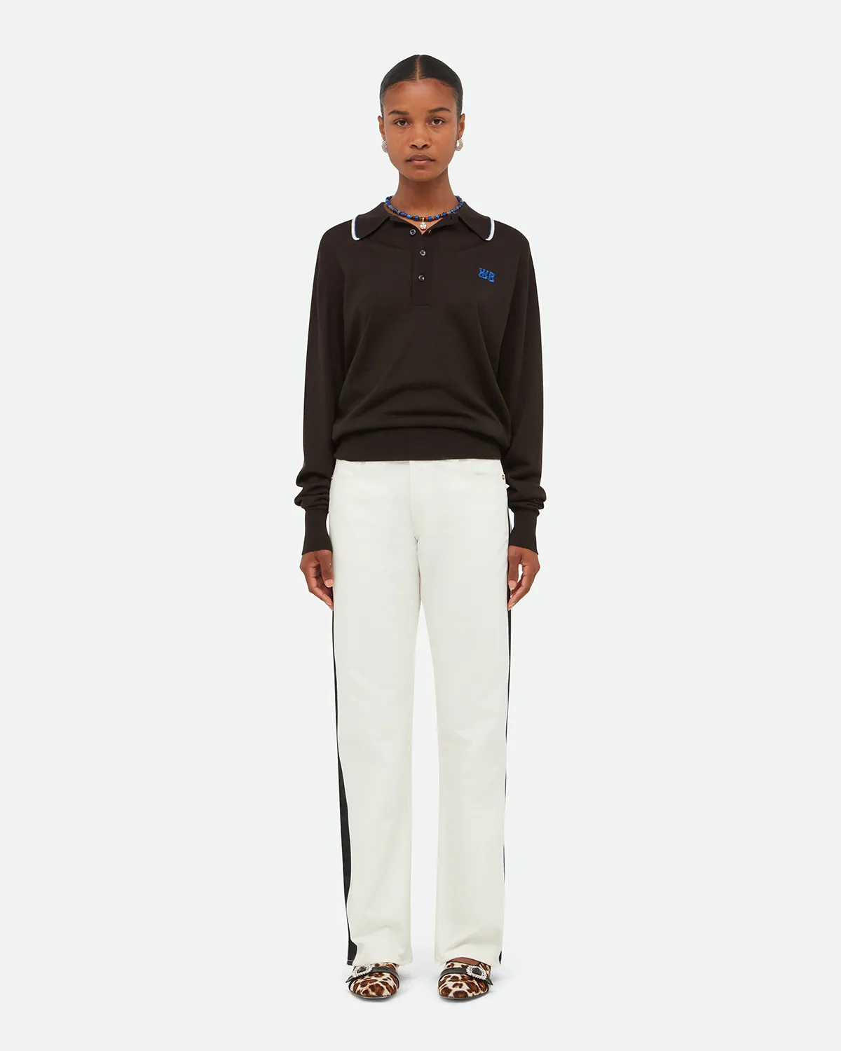 Woman wearing black long-sleeve polo, white pants with black side stripes, and animal-print shoes.