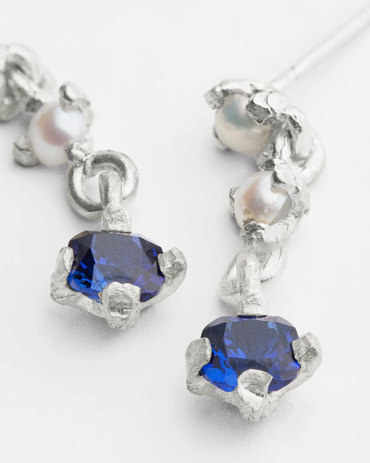 Silver earrings with blue gemstones and small pearls on a white background.