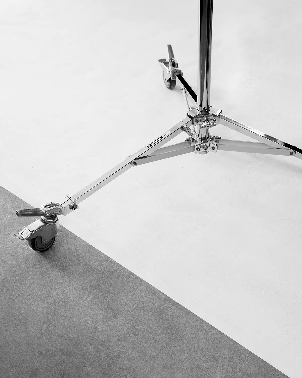 Close-up of a chrome LRP tripod stand with wheels on a white and gray floor.