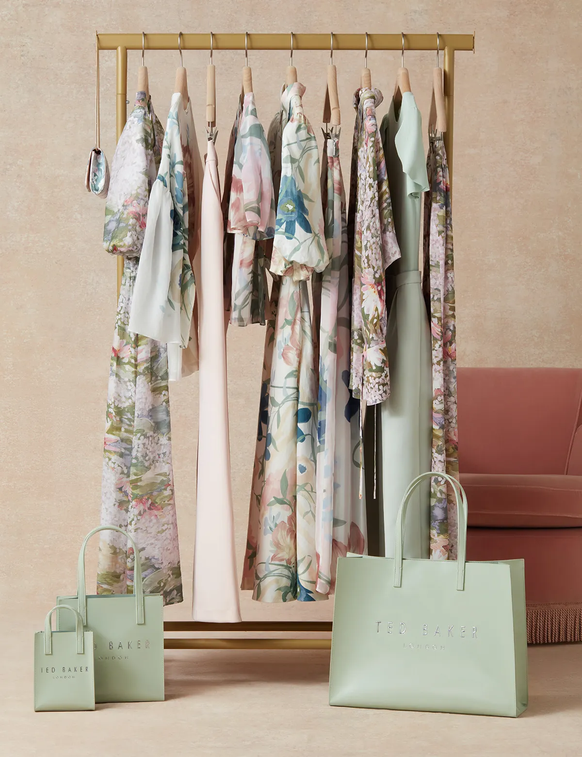 Clothing rack with pastel floral dresses and three green Ted Baker London shopping bags in front.