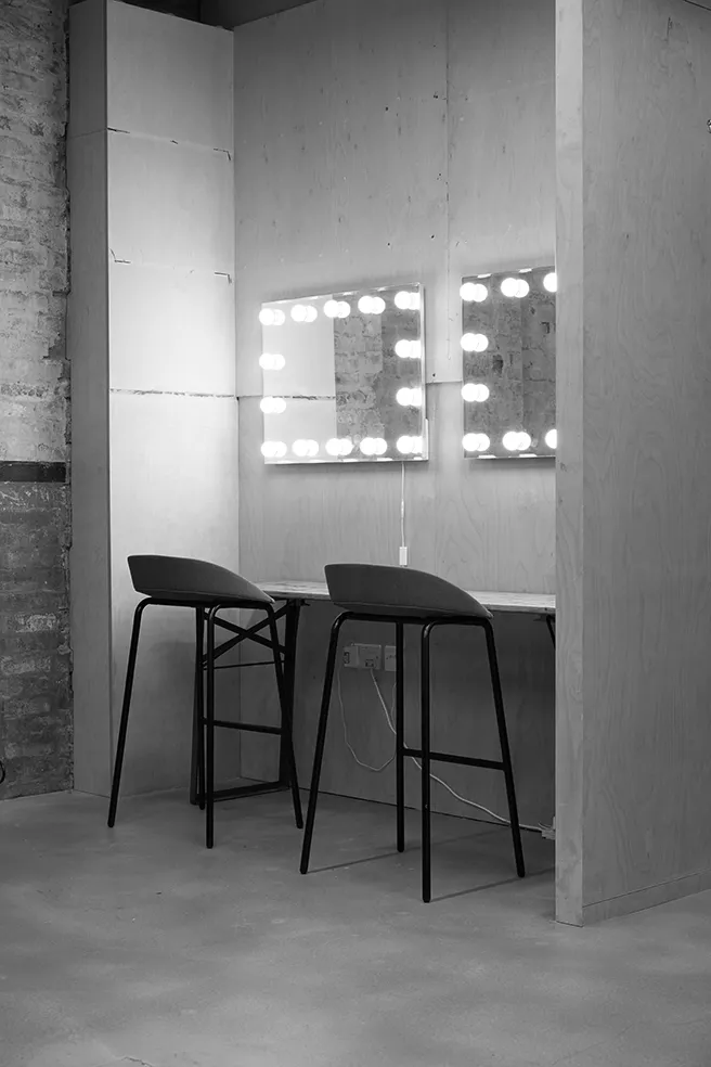 Black and white image of a minimalist makeup station at LRP studios, featuring two illuminated vanity mirrors and modern black stools, used to prepare models for eCommerce photography.