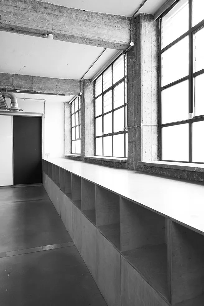 Black and white image of a brightly lit industrial space at LRP studios, featuring large factory windows and a built-in wooden storage bench used during eCommerce photography shoots.