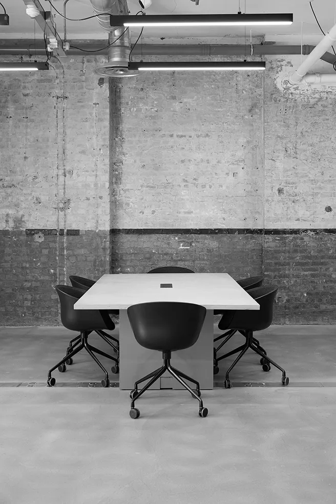 Black and white image of an industrial meeting area at LRP studios, featuring a light rectangular table and black swivel chairs, used as a workspace during eCommerce photography shoots.