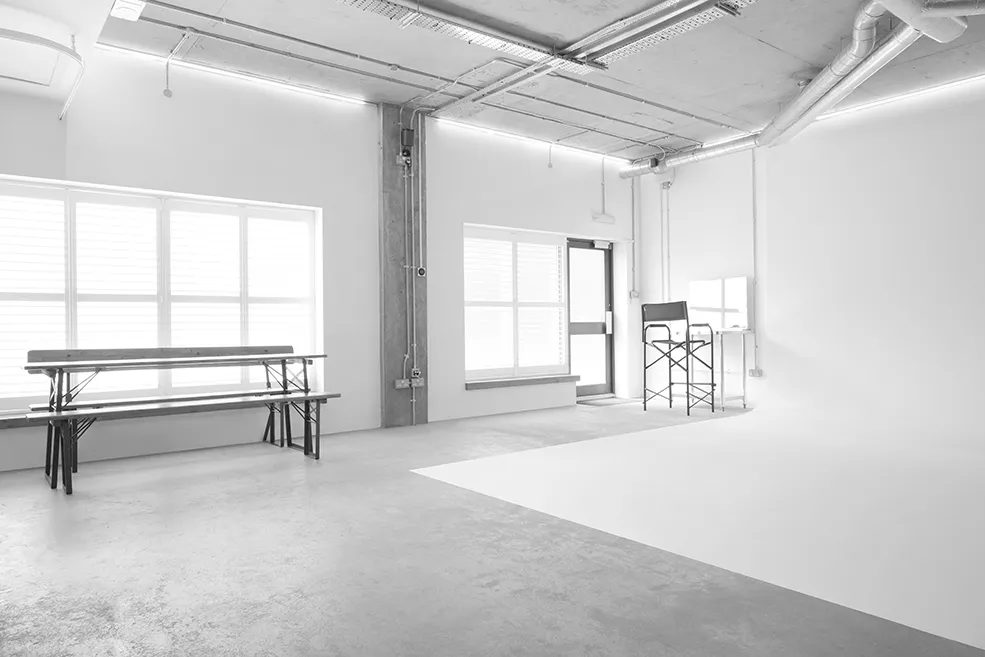 Black and white image of a bright, industrial studio space at LRP studios, featuring a large white infinity cove, a trestle table, and a styling station for eCommerce photography.