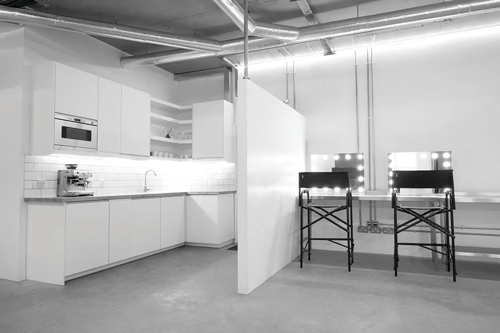 Black and white image of a preparation area at LRP studios, featuring a modern white kitchenette alongside a partitioned makeup station used by eCommerce photography teams.