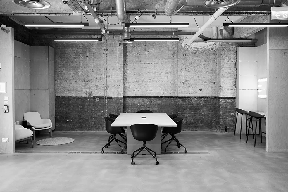 Black and white wide shot of a multi-purpose industrial workspace at LRP studios, featuring a central meeting table, lounge seating, and a makeup station designed for eCommerce photography teams.