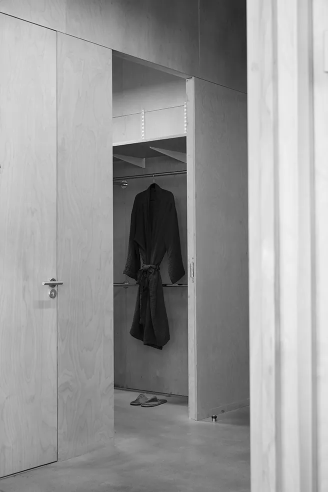 Black and white image of an open plywood wardrobe with a hanging dark robe and slippers at LRP studios, providing model amenities during eCommerce photography.