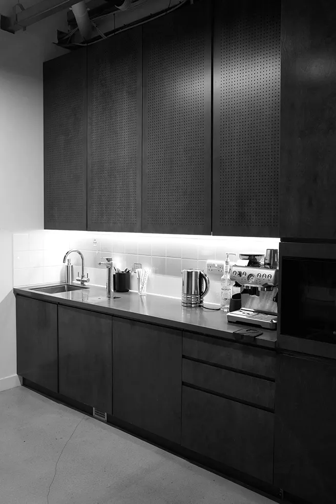 Black and white image of a modern, dark-toned kitchenette equipped with an espresso machine at LRP studios, providing refreshments for eCommerce photography teams.