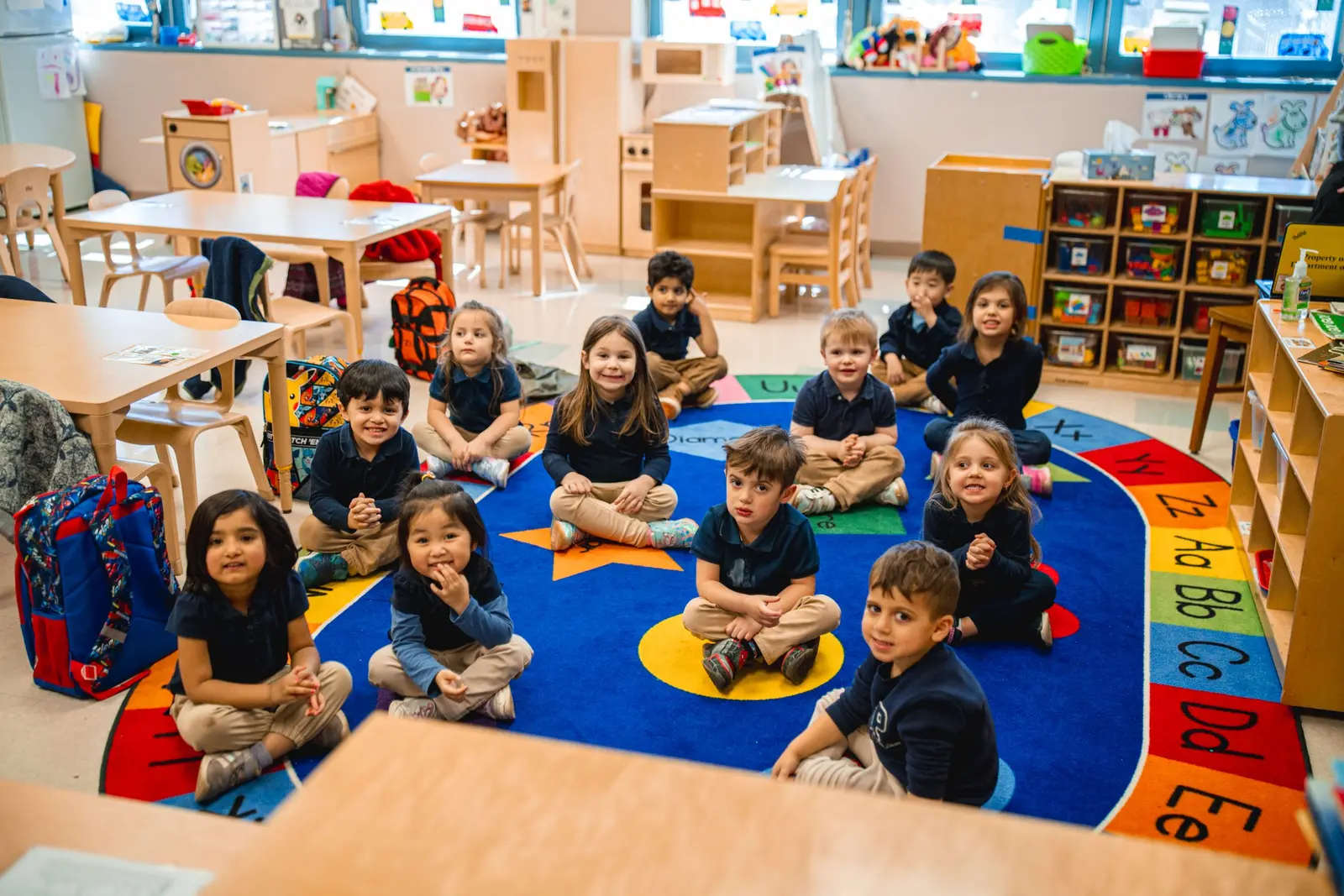 Kindergarten students sitting together on an alphabet rug in classroom