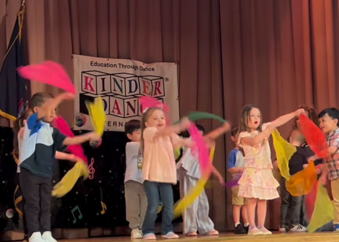 Young students waving colorful scarves during a KinderDance stage performance
