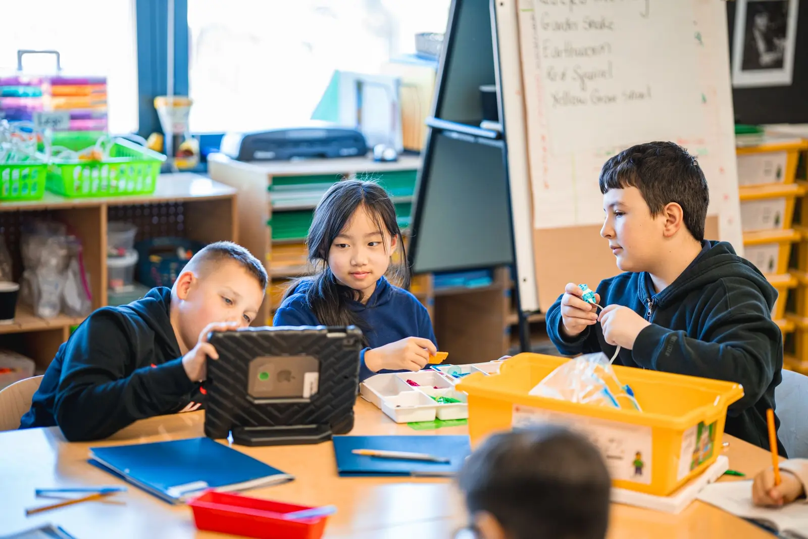 Three students collaborating with tablet and materials at classroom table